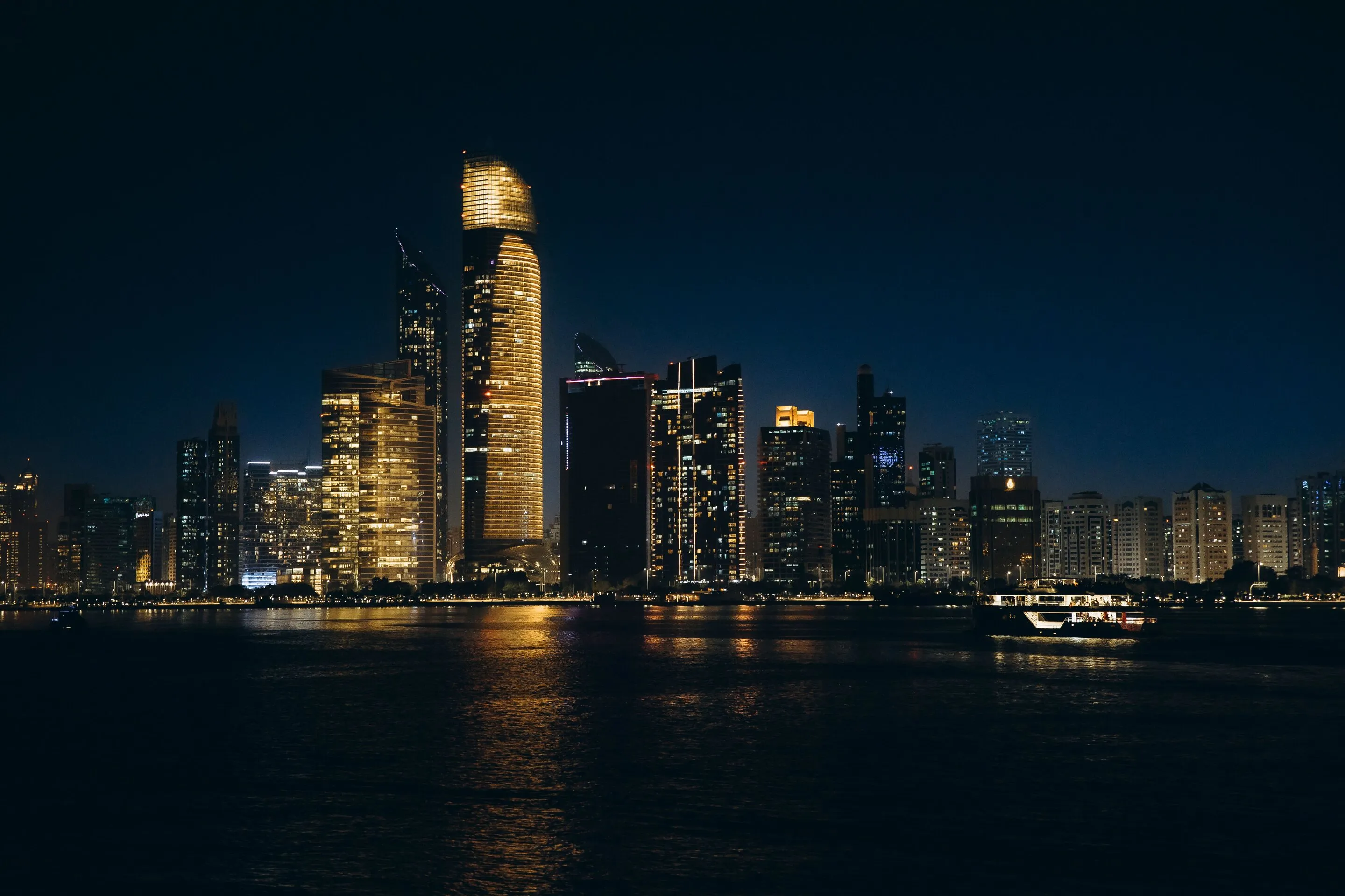 Abu Dhabi waterfront towers glowing gold at dusk, reflected across the harbour water